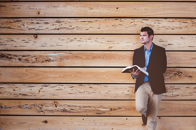 Muž s knihou v ruke stojí pri drevenej stene a pozerá do diaľky.jpg
